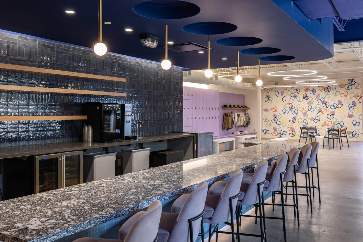 Modern lounge with a marble bar and high-back chairs, abstract mural, and social vibe with hanging round lights.