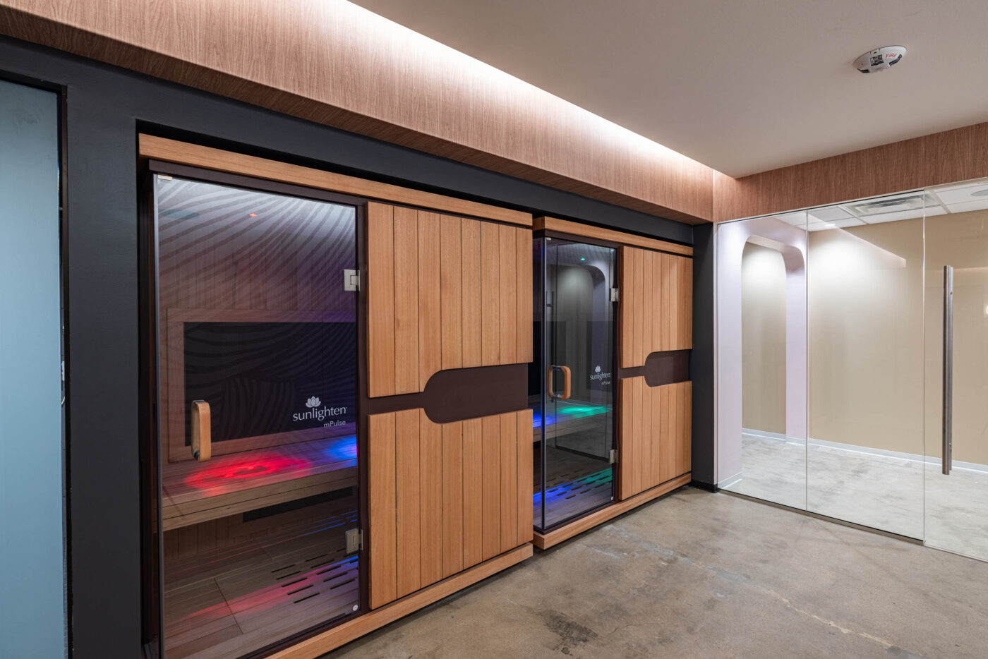A modern sauna with wooden paneling and interior LED lighting, fostering social connections, next to glass doors and a polished concrete floor.