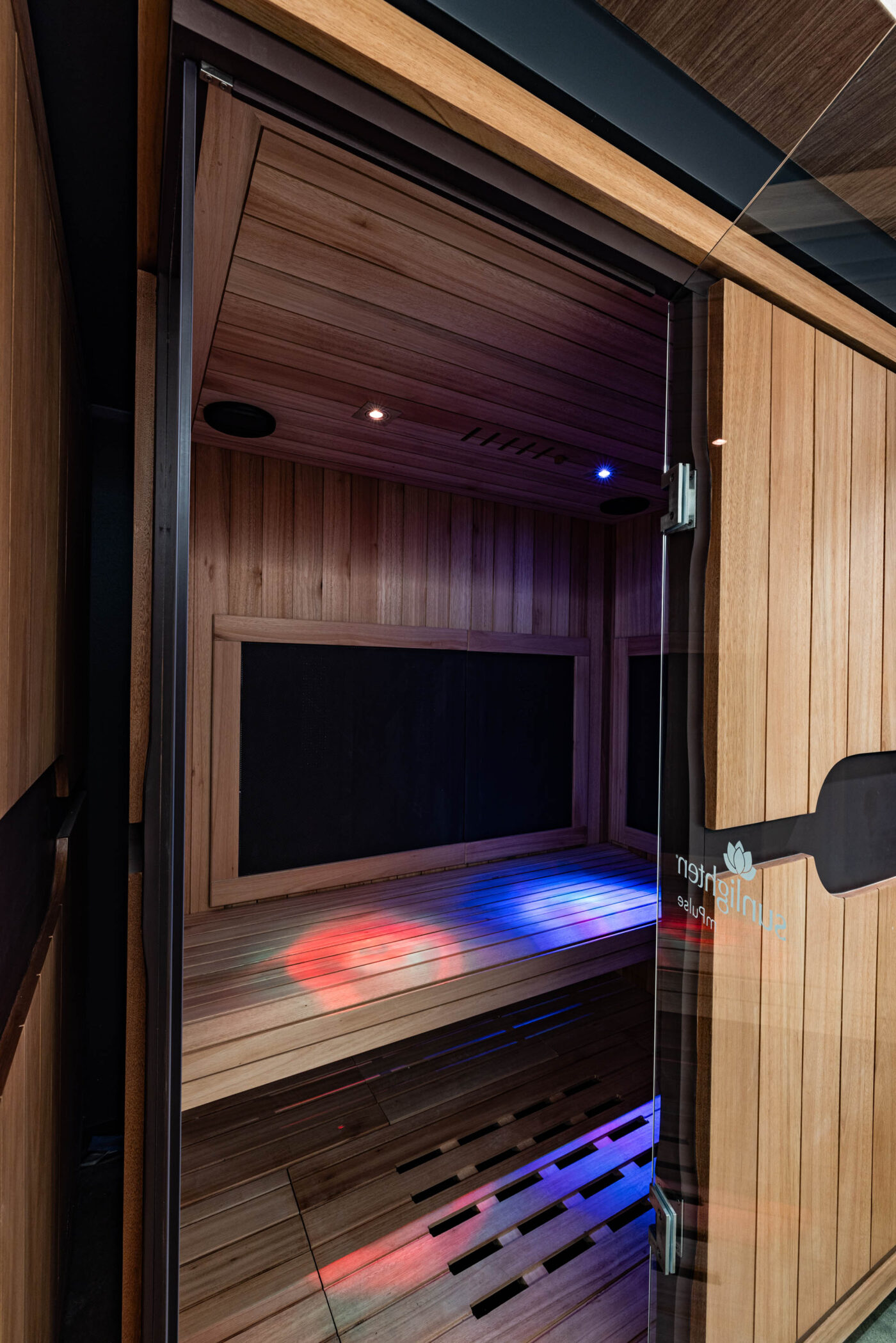 Wood-paneled sauna interior with mood lighting for a social setting, viewed through a glass door.