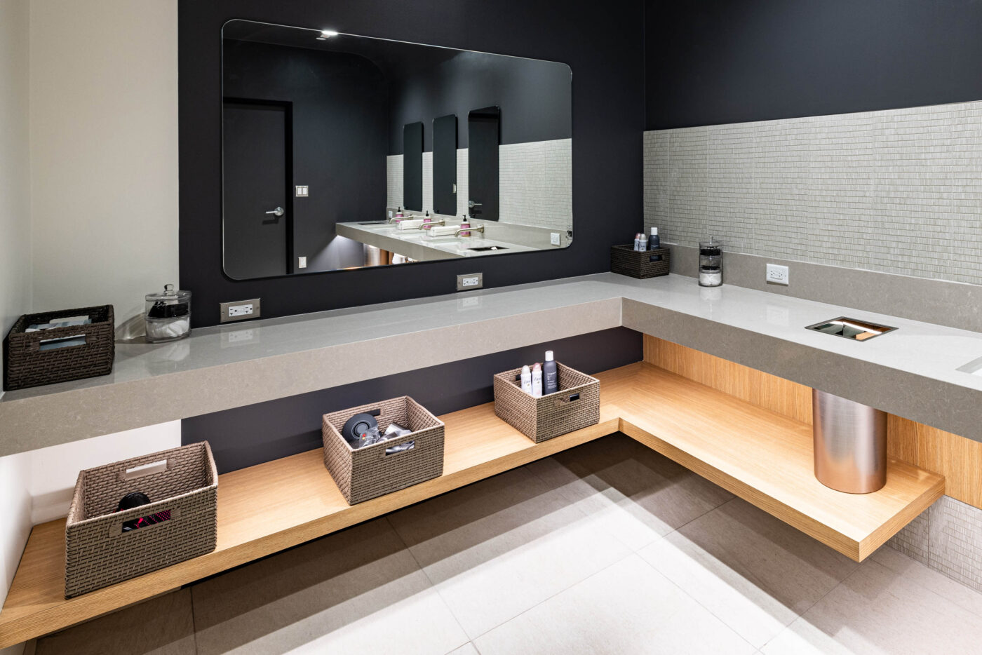 Modern bathroom with a large mirror, gray counter, wicker baskets, fitness vibe, stainless steel bin, and black-and-white walls.