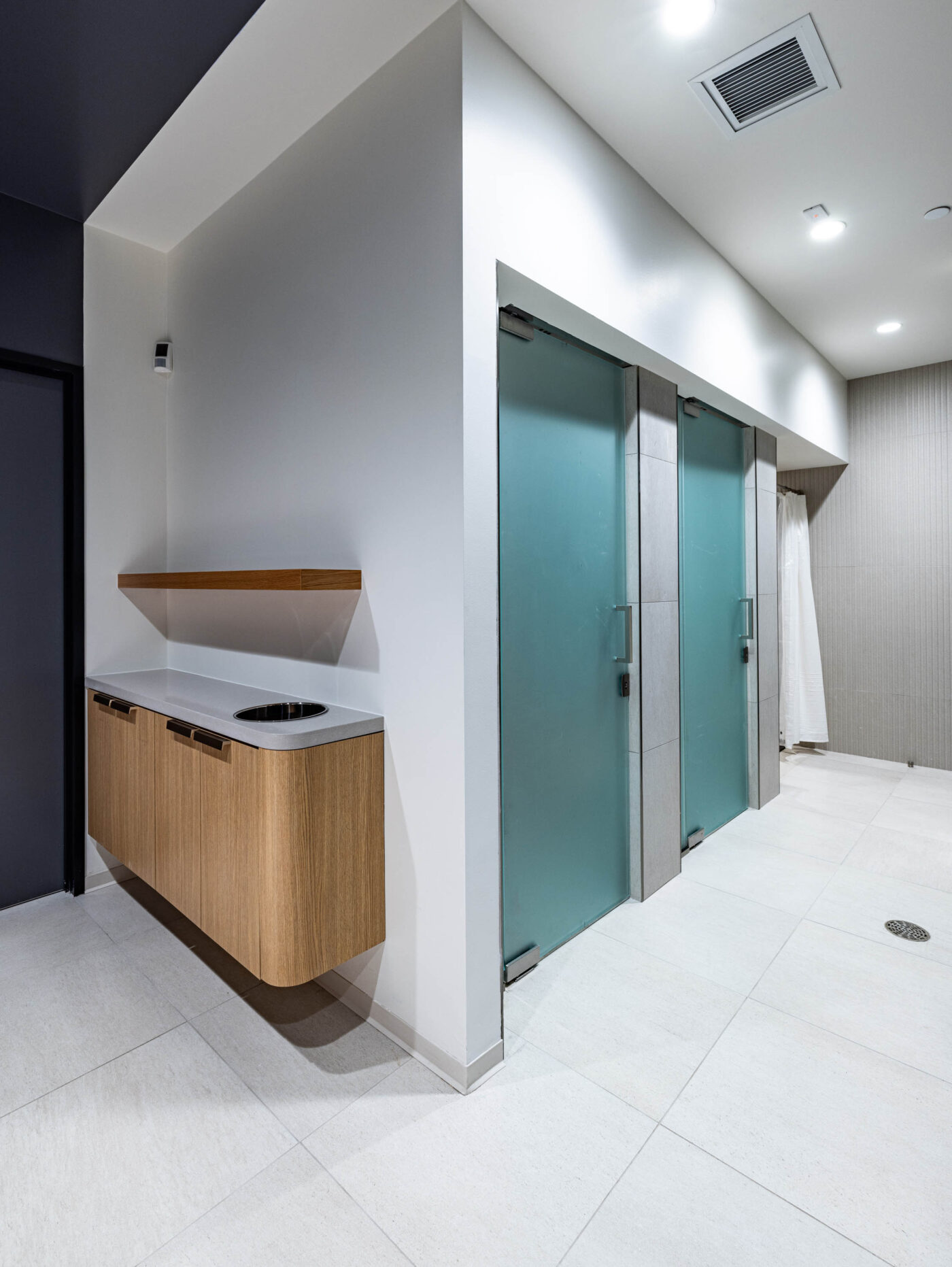 Modern restroom with two frosted glass doors, a wooden sink counter with a white basin, and overhead lighting—a social oasis.