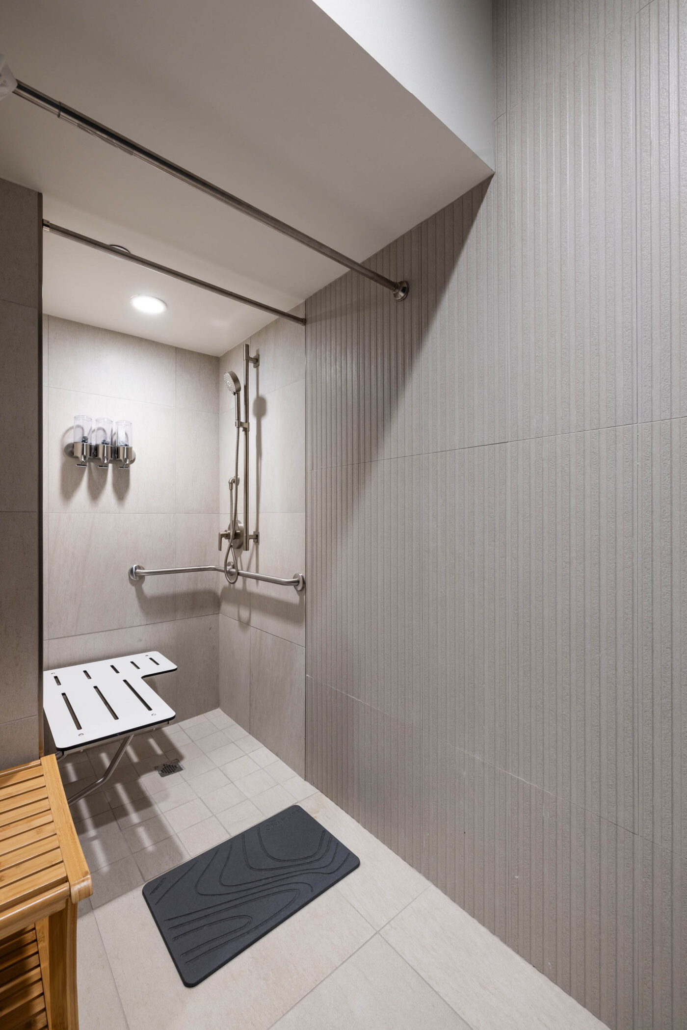 Accessible shower ideal for fitness enthusiasts, featuring a mounted seat, grab bars, soap dispensers, and a rubber mat.