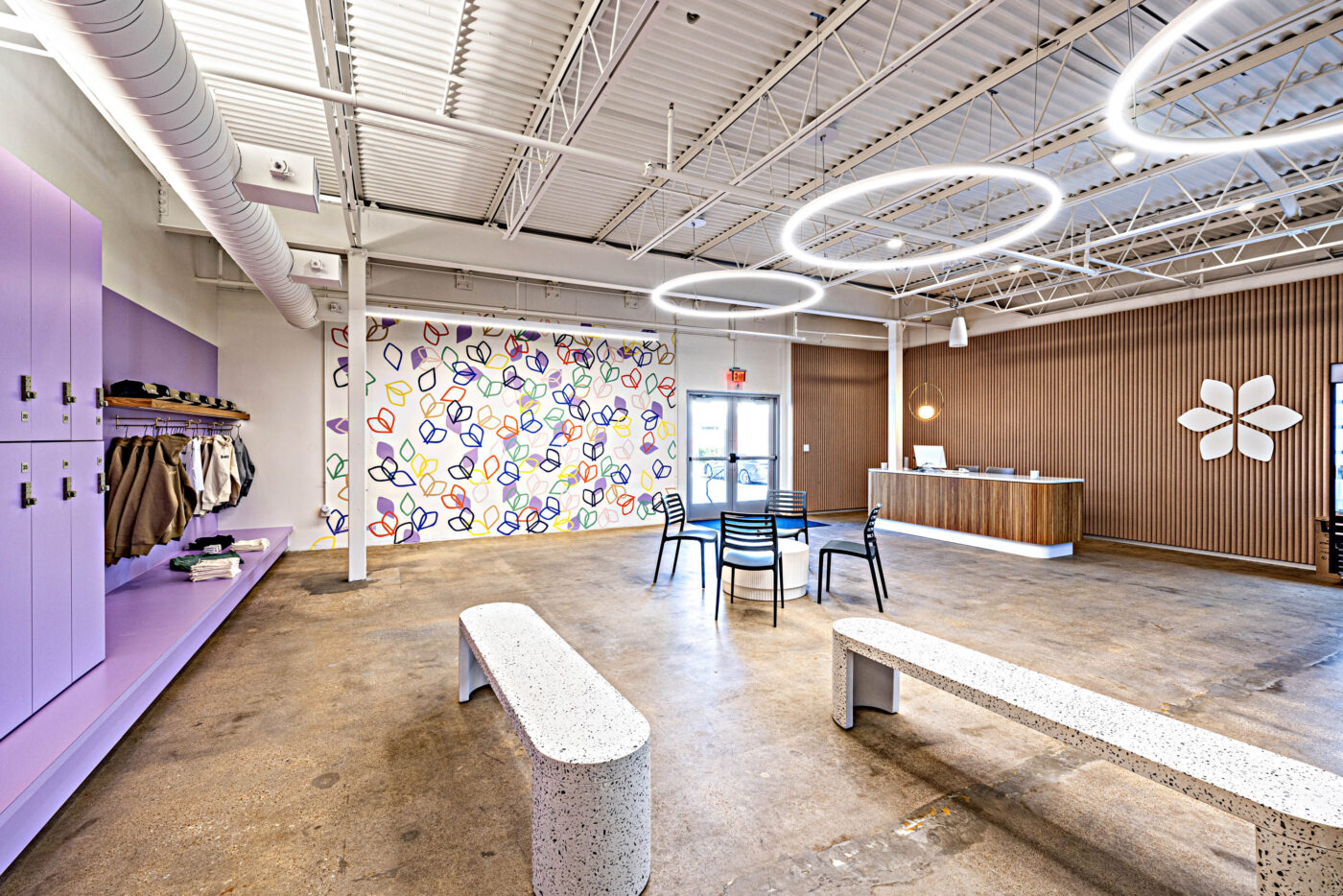 Spacious modern lobby with fitness-focused purple lockers, abstract wall art, reception desk, and terrazzo benches.