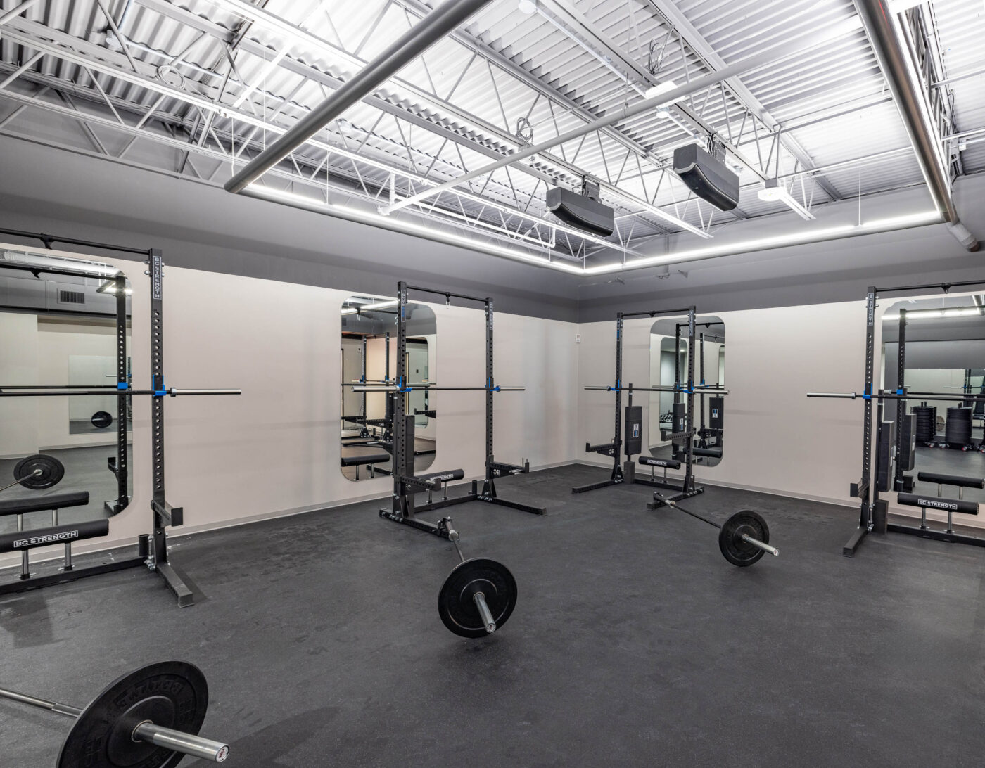 Brightly lit fitness room with multiple squat racks, barbells, and mirrors, perfect for a dynamic workout.