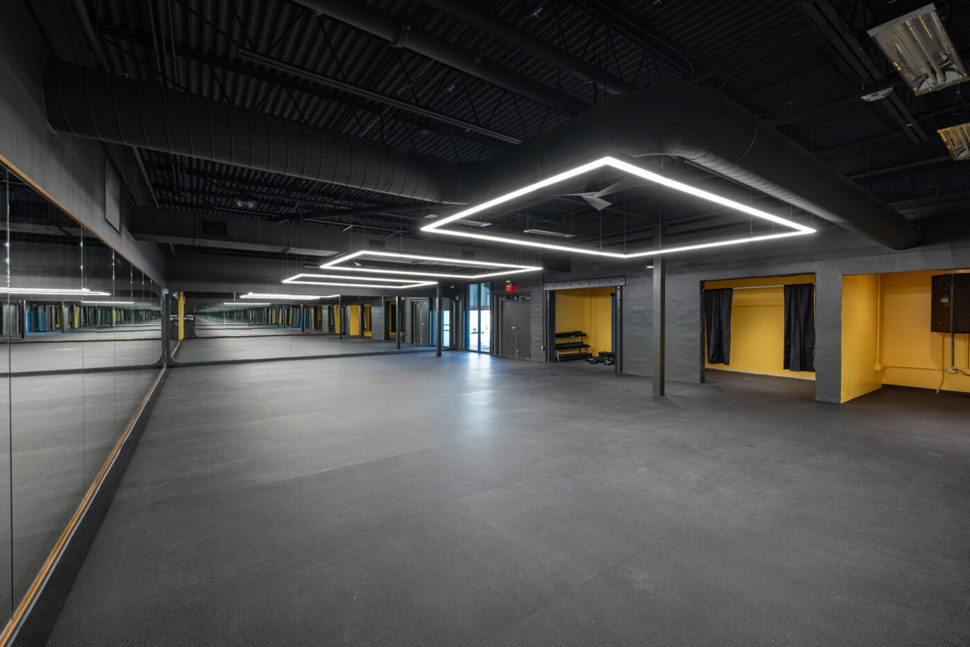 Empty dance studio with dark flooring, mirrored wall, yellow accents, and lights creating square patterns for fitness enthusiasts.