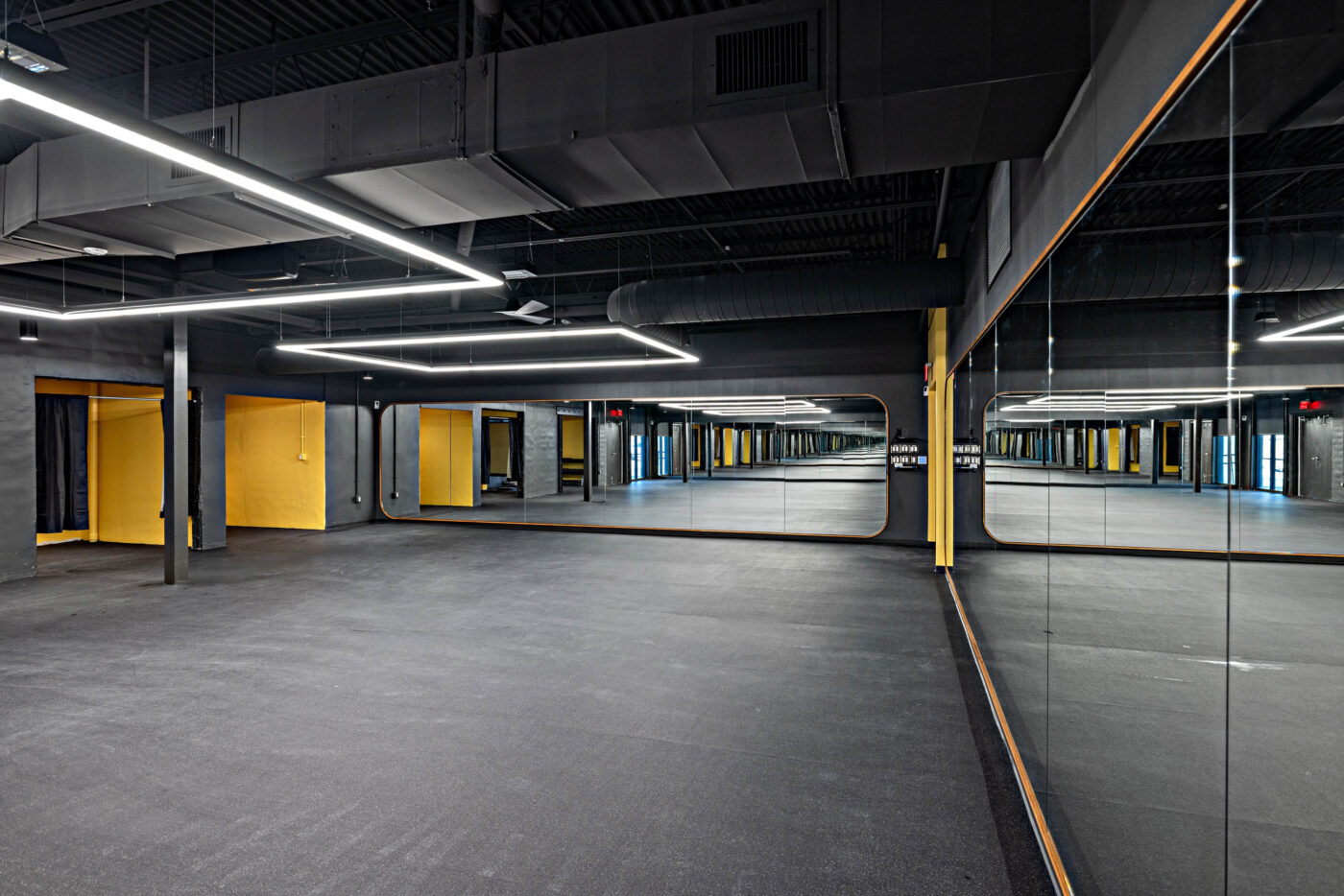 Empty gym studio with mirrored walls, yellow accents, and overhead lighting—perfect for social fitness sessions.