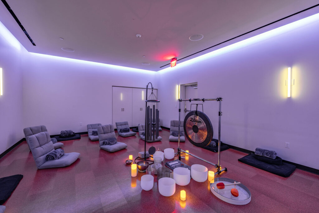 A dimly lit meditation room with floor cushions, a gong, singing bowls, and soft glowing candles sets the stage for yoga.