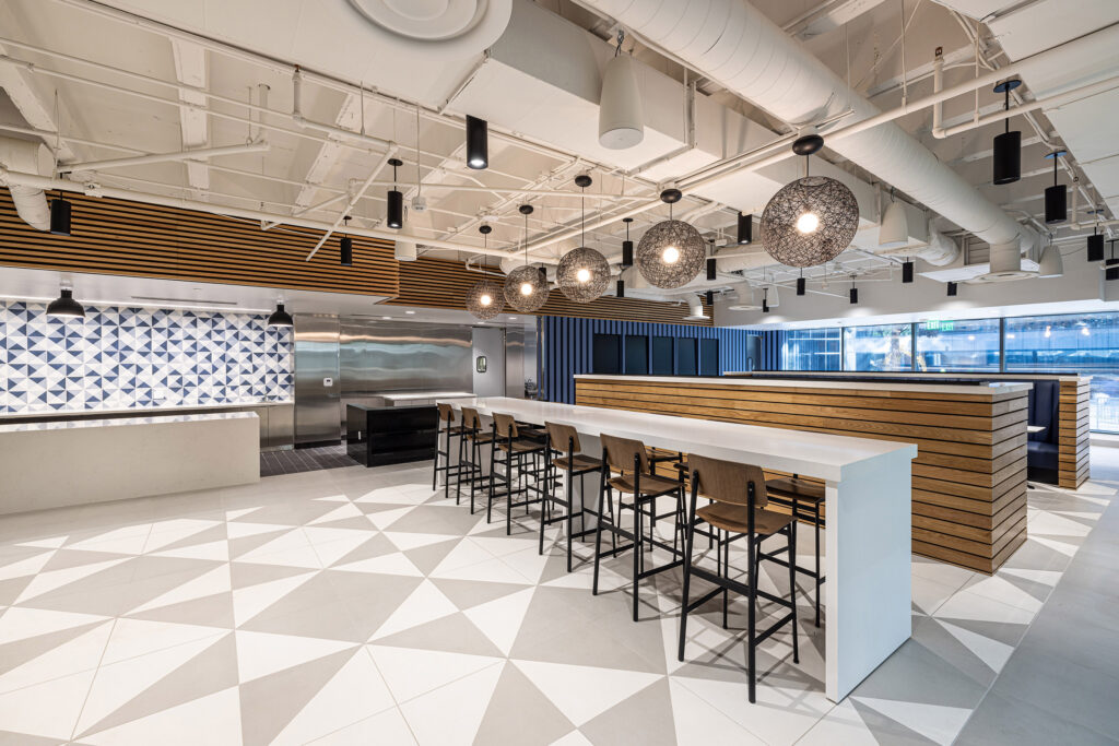 Park West Cafe break room with long tables, wooden chairs, geometric flooring, pendant lights, and patterned wall tiles.