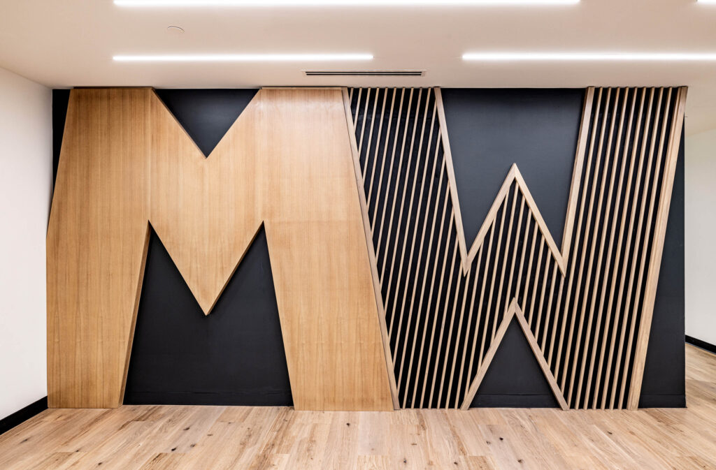 Large wall art showcasing wooden letters MW for Michael Walker on a black background with vertical slats on the right.