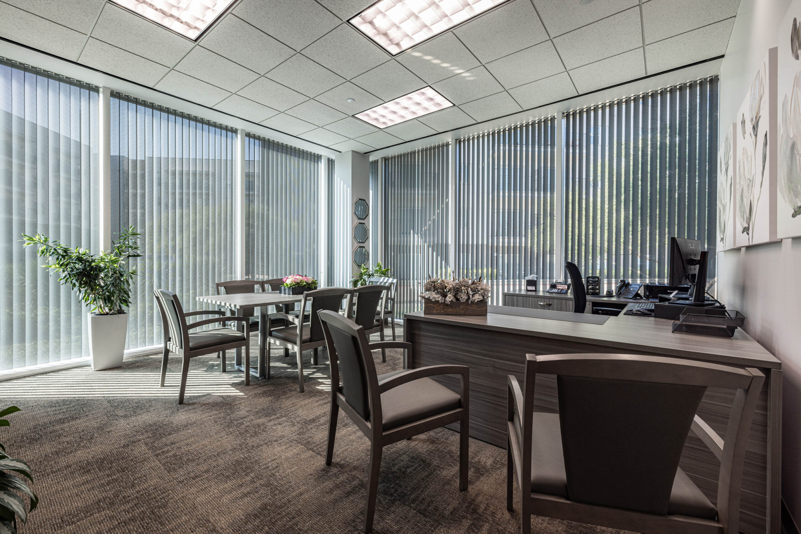 Modern office with a desk, chairs, and a table. Large windows overlook the Tollway, letting in natural light. Decor includes plants.