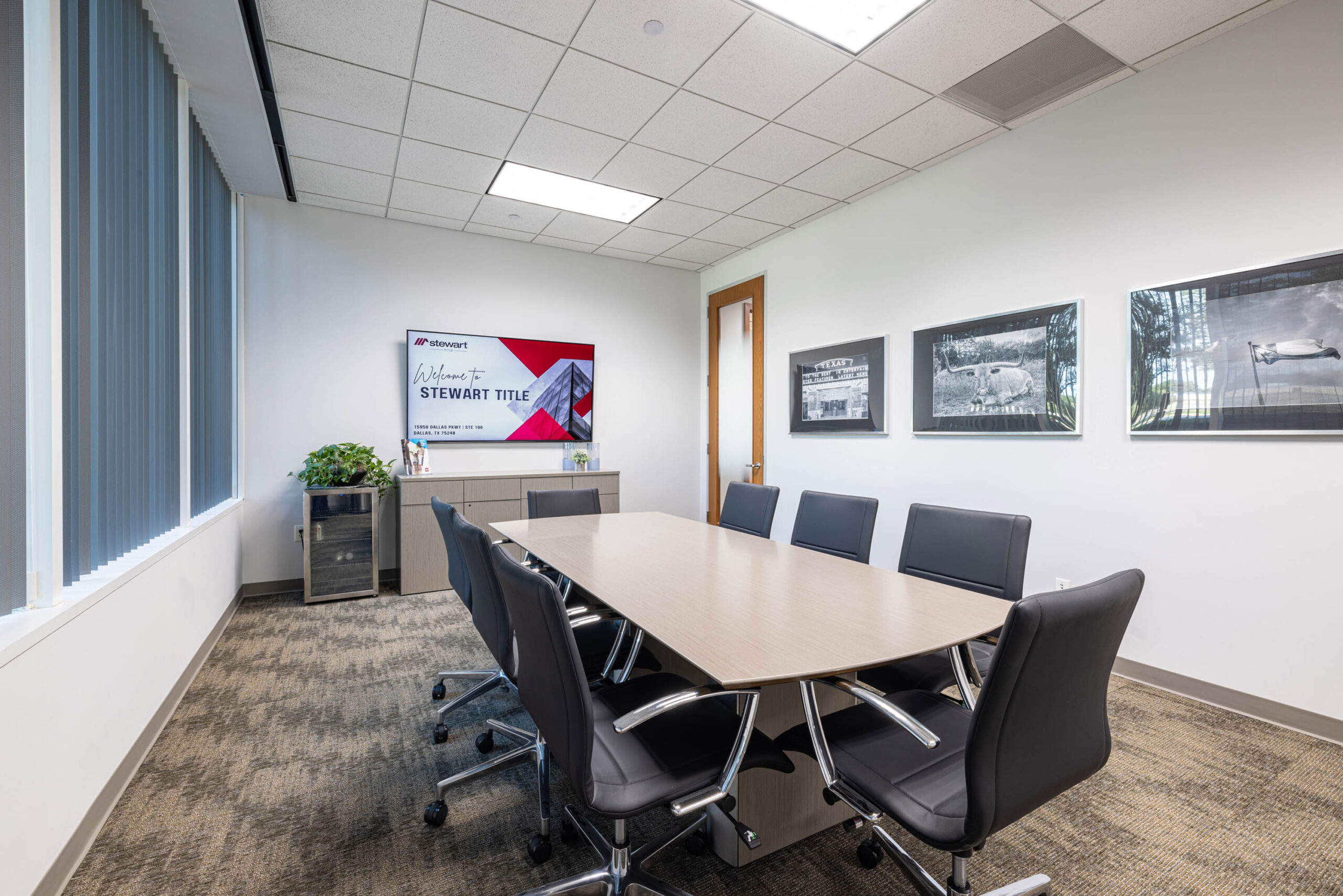 Modern conference room with black chairs around a wooden table, art on walls, and a screen displaying Stewart Titles logo.
