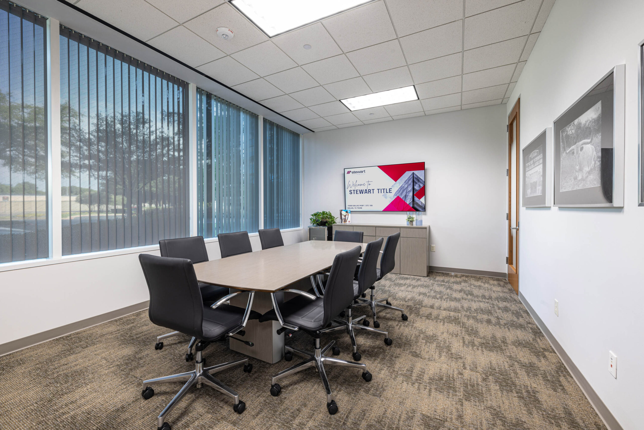 Modern conference room with a long table, Tollway view, black chairs, wall art, and large windows with vertical blinds.
