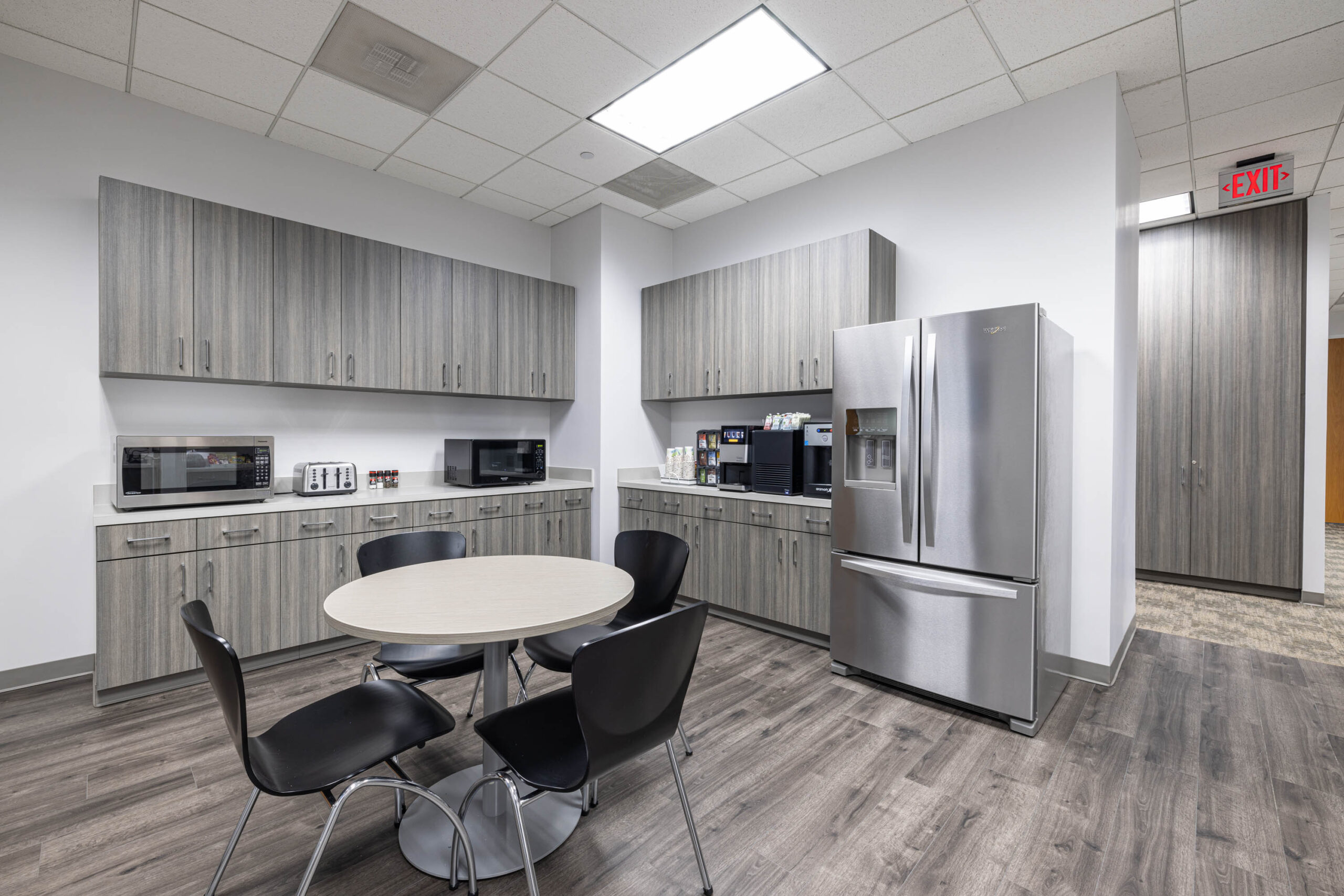Modern office kitchenette near Tollway with round table, four chairs, stainless steel fridge, microwaves, and cabinetry.