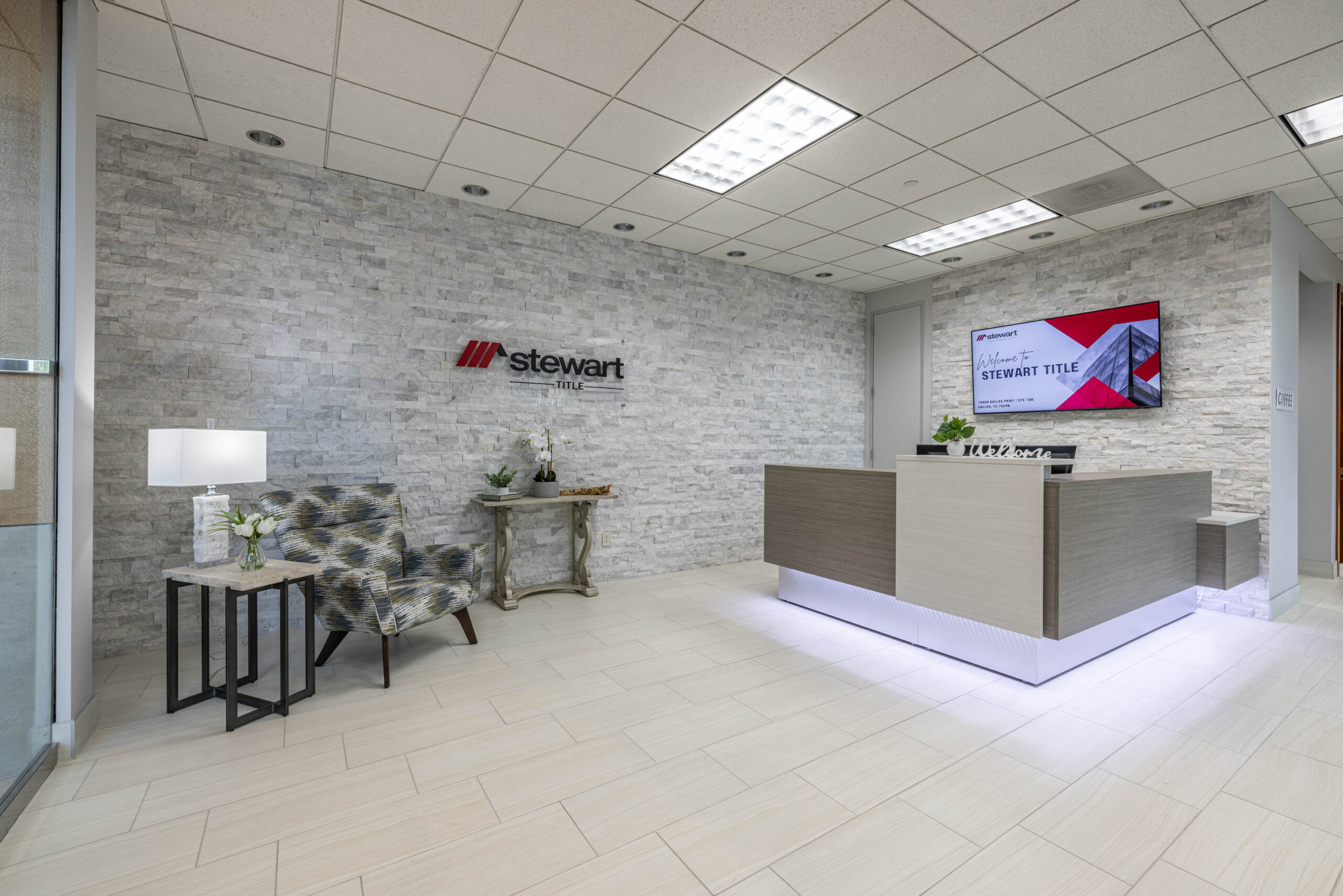 Modern office lobby with a stone accent wall, a Tollway map behind the reception desk, and a patterned armchair by the lamp.