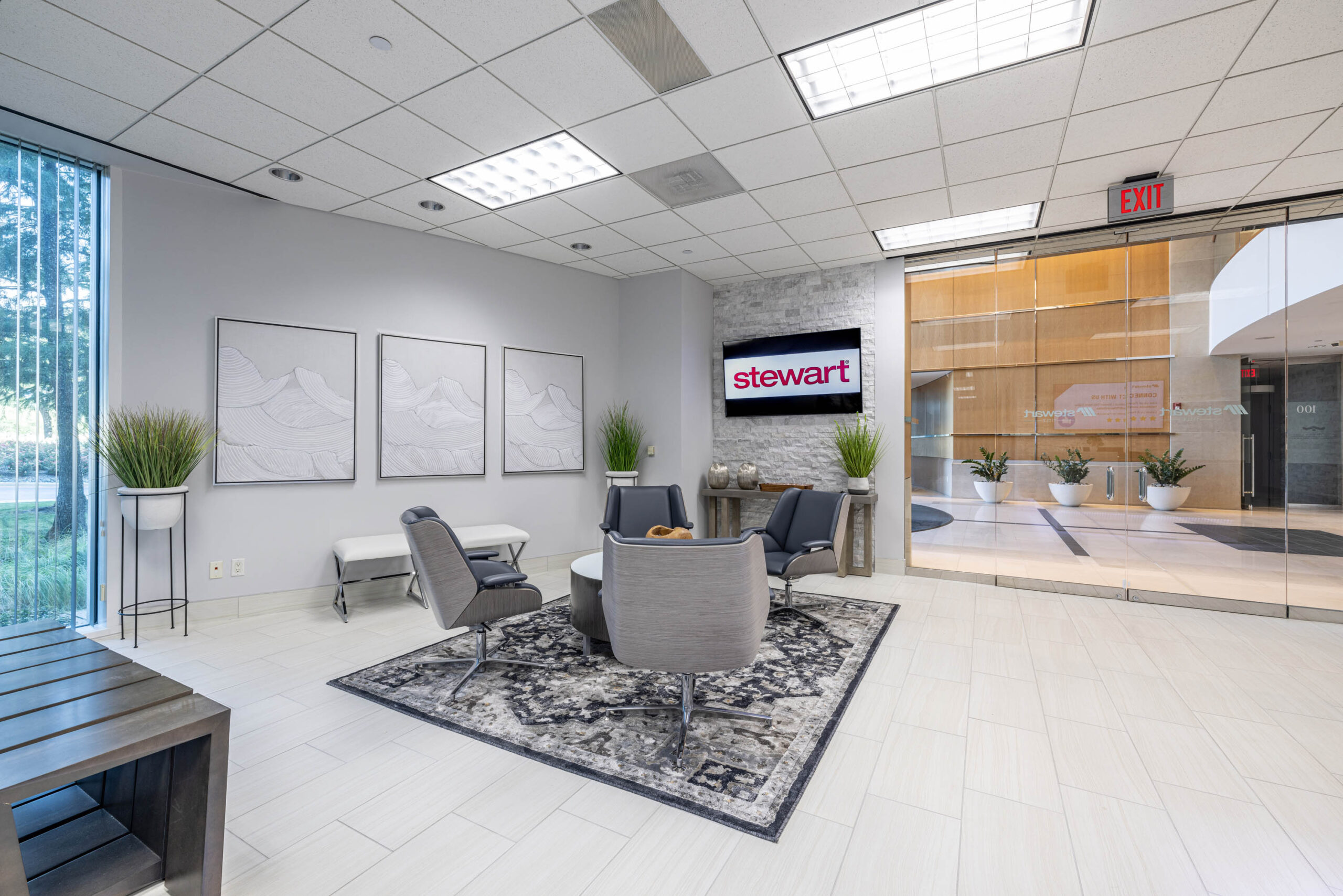 Modern office lobby with gray chairs, a round table, and wall art beneath a Stewart Title sign. Glass doors reveal the Tollway.