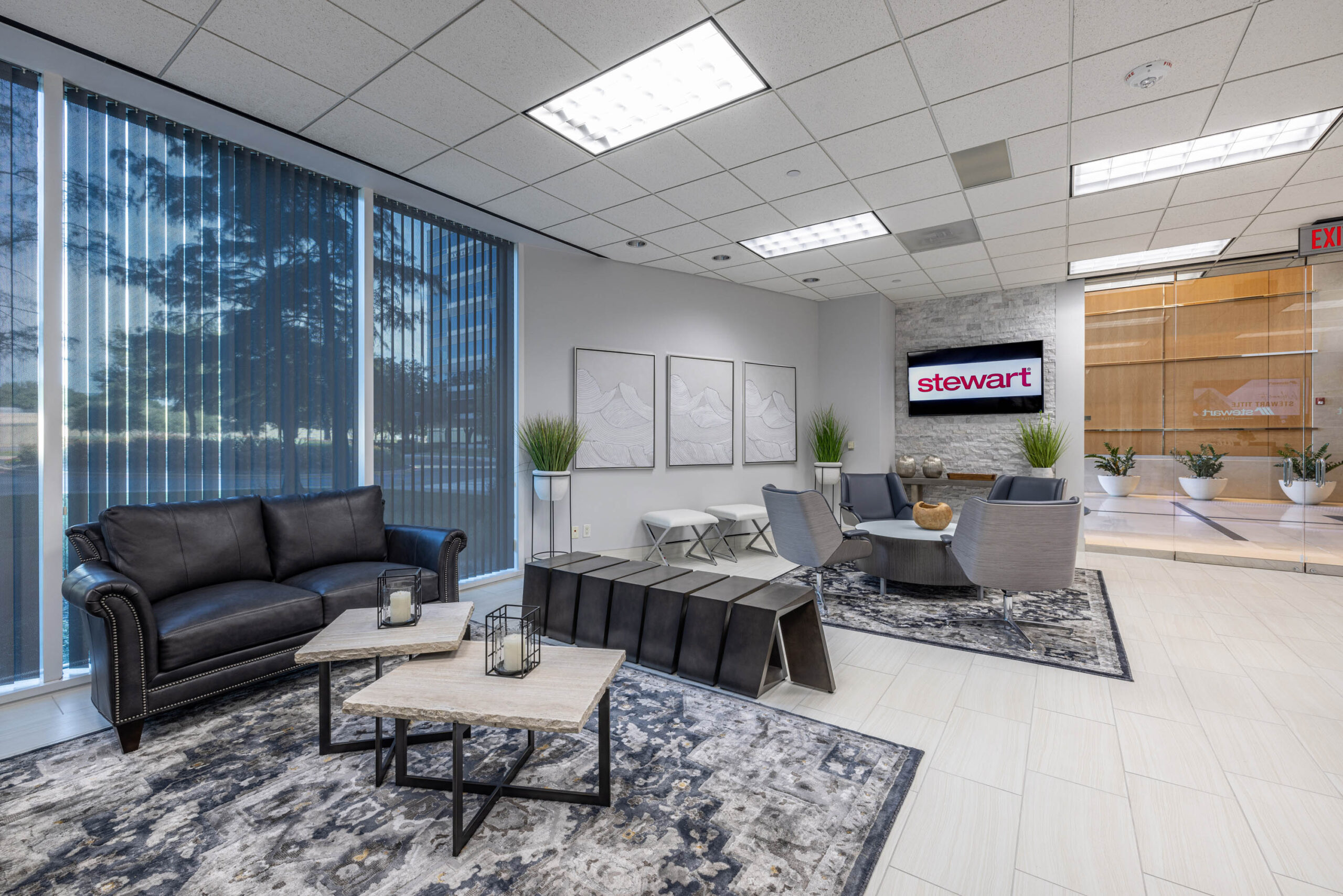 Modern office lobby with black leather sofa, abstract art, and a wall-mounted screen in Stewart Titles Tollway building.