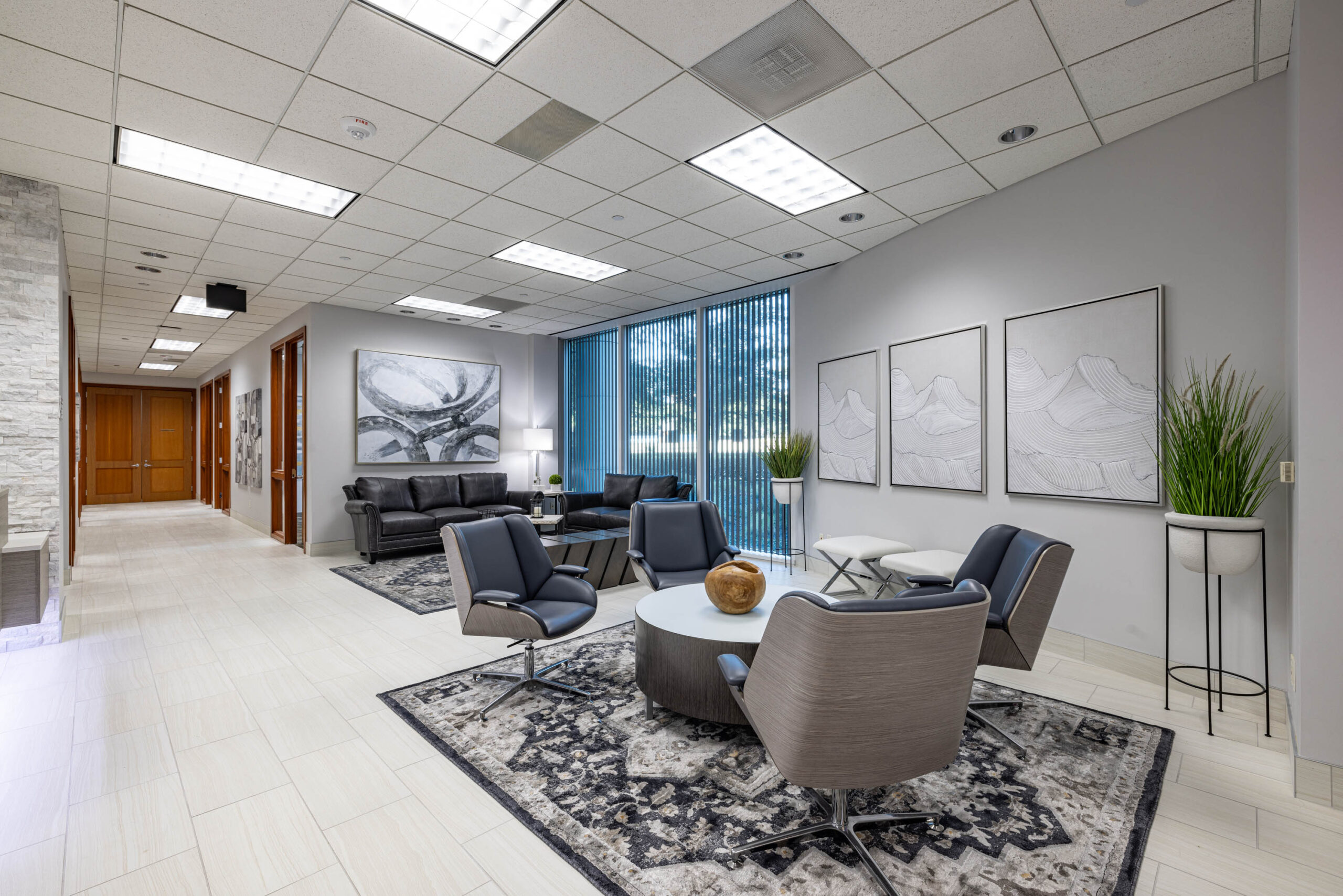 Modern office lobby with gray chairs, black sofas, abstract art, green plants, and large windows overlooking the tollway.
