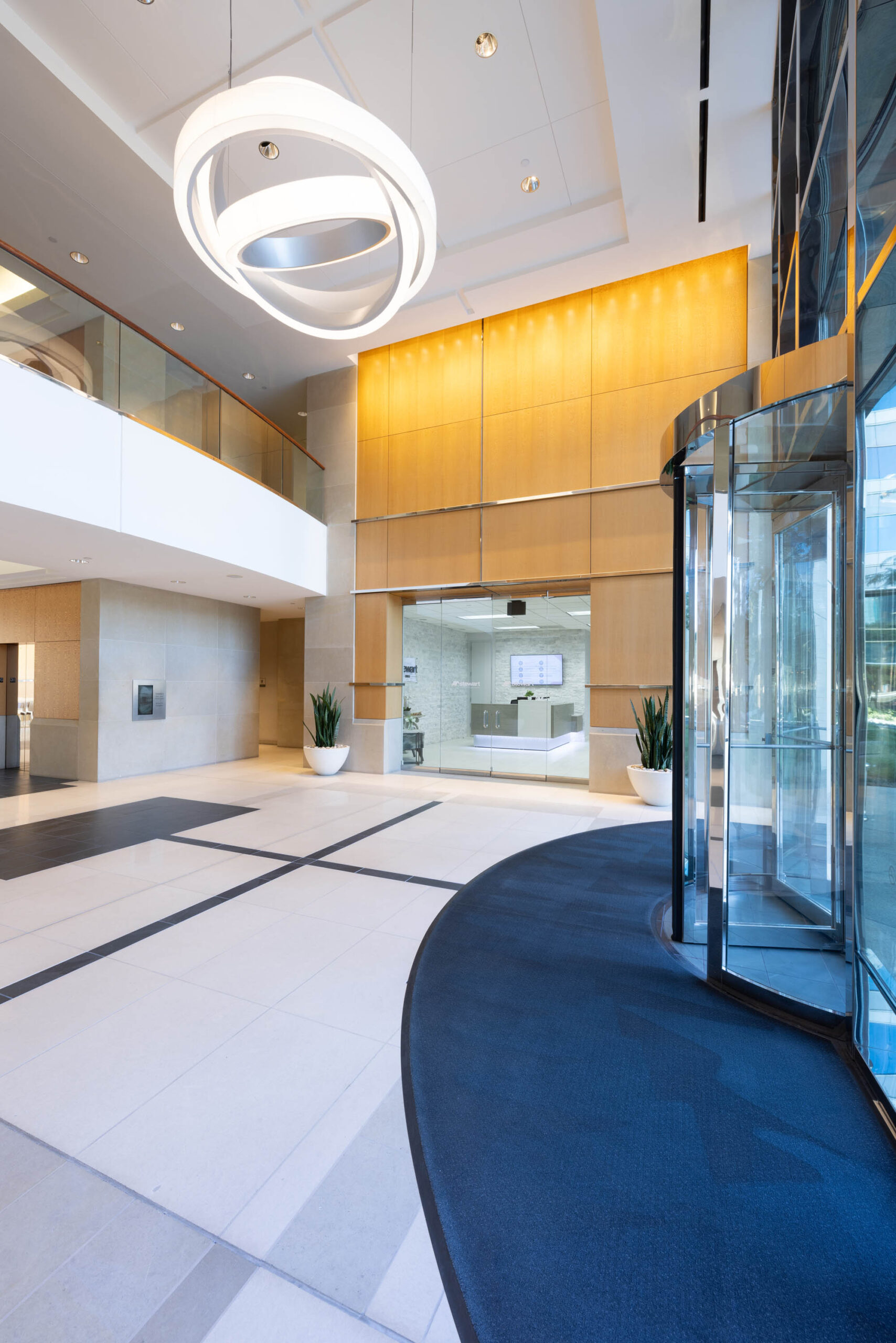 Modern building lobby with a revolving glass door, geometric ceiling light, and beige wall paneling near the Tollway.