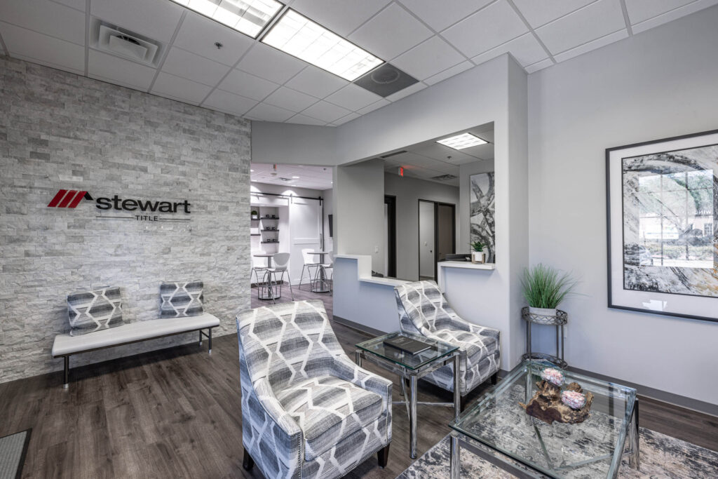 Modern Plano office lobby with gray chairs, glass tables, a stone accent wall featuring the Stewart Title logo, and abstract artwork.