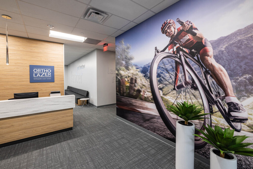 Office lobby with a cyclist mural on the wall. Reception desk on the left, plants in the foreground.