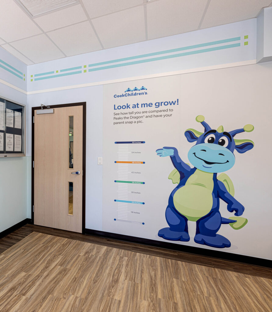 Wall with height chart featuring a friendly blue dragon illustration, beside a wooden door at Southlakes Cooks restaurant.