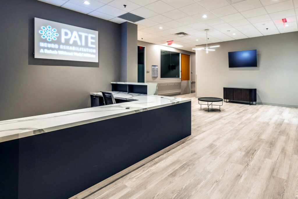 Modern office reception area with a desk, chairs, overhead sign, TV, and round table on wooden flooring.